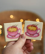 An adult's hand holding up two tiles from the Bajo Wooden Tiles Memory Game. The tiles have an illustration of a pink dotty teacup on them. These heirloom quality toys by Bajo are part of a wide range of wooden toys available here at Babipur. 