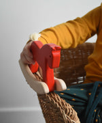 A close up of a child's hand holding a red coloured Bajo Mini Rocking Horse. The child is sitting in a wicker chair. These heirloom quality toys by Bajo are part of a wide range of wooden toys available here at Babipur. 