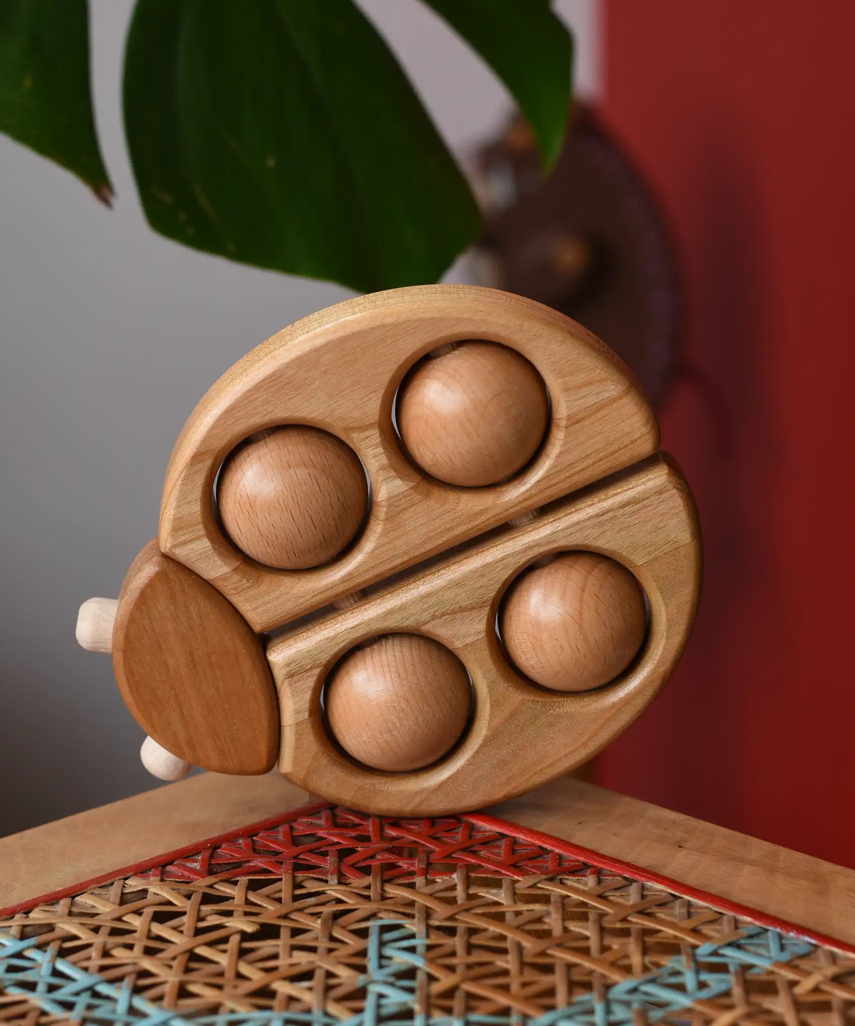 Bajo natural wooden ladybird teether  placed on a rattan stool in the Babipur playroom.