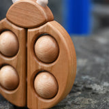 Close up of the Bajo natural wooden ladybird teether placed on a stone wall outdoors in the Babipur garden.