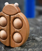 Close up of the Bajo natural wooden ladybird teether placed on a stone wall outdoors in the Babipur garden.