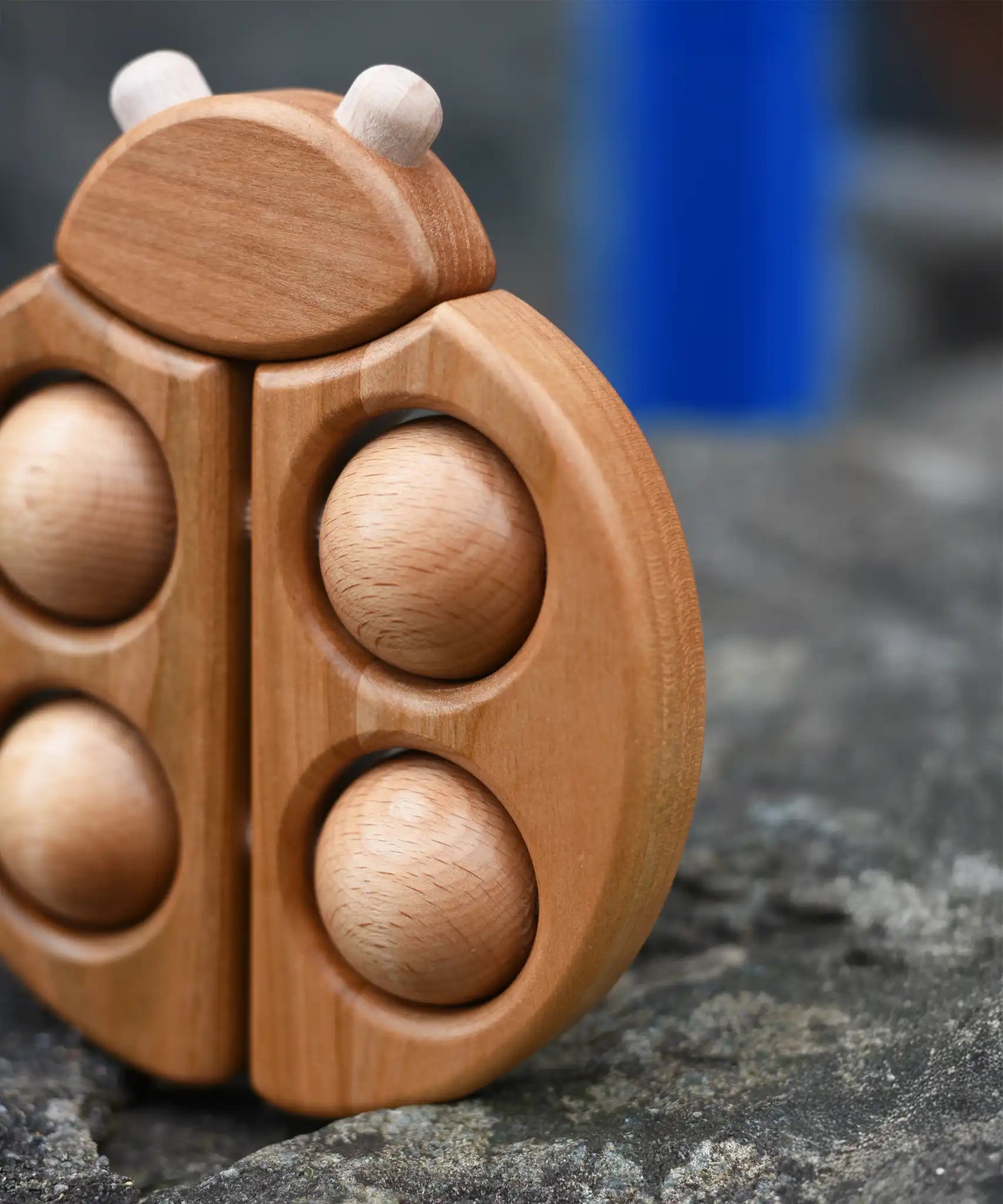 Close up of the Bajo natural wooden ladybird teether placed on a stone wall outdoors in the Babipur garden.