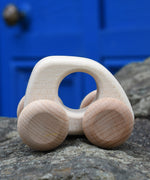 Bajo hand made wooden natural mini style car available at Babipur. Features matching unpainted wheels and a cut out hole for easy grabbing. Photo is in a outdoor setting 