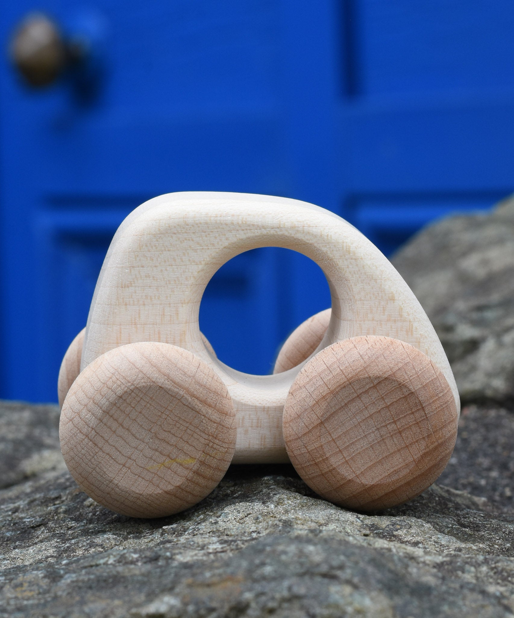 Bajo hand made wooden natural mini style car available at Babipur. Features matching unpainted wheels and a cut out hole for easy grabbing. Photo is in a outdoor setting 