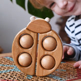 Bajo natural wooden ladybird teether  placed on a rattan stool in the Babipur playroom with a child looking on in the background.