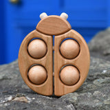 Bajo natural wooden ladybird teether placed on a stone wall outdoors in the Babipur garden.