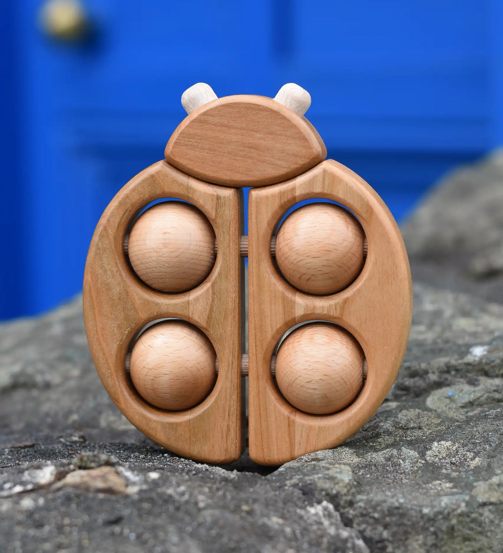 Bajo natural wooden ladybird teether placed on a stone wall outdoors in the Babipur garden.