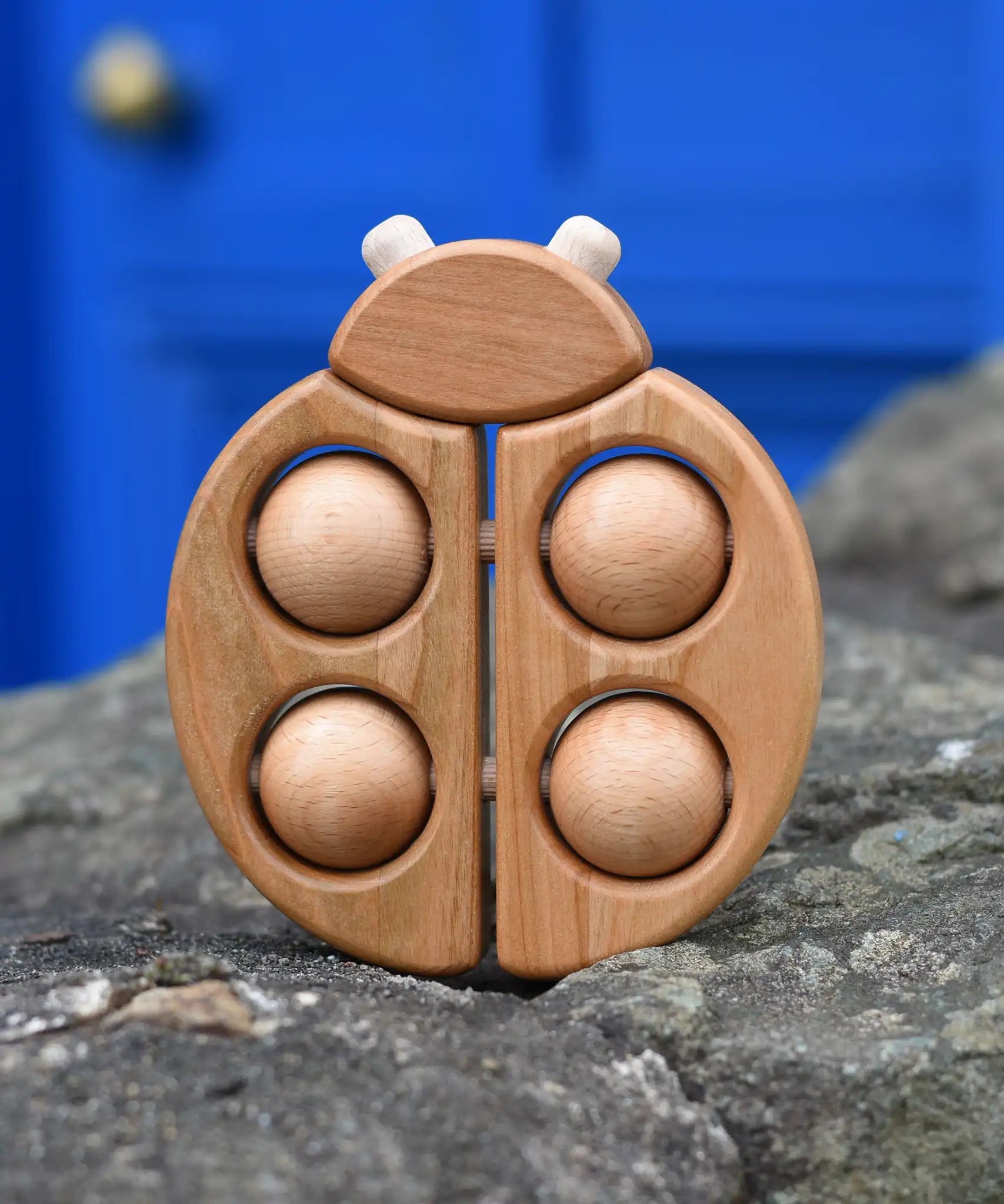 Bajo natural wooden ladybird teether placed on a stone wall outdoors in the Babipur garden.