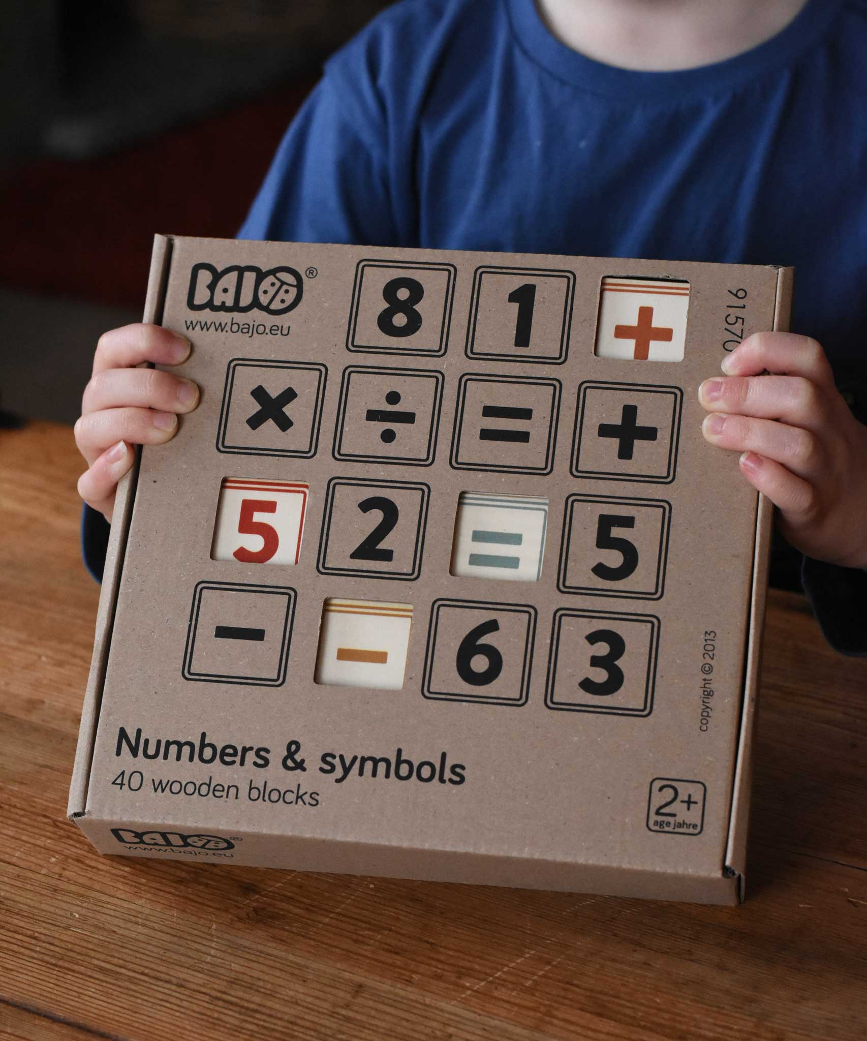 A child holding up the box of Bajo 40 Numbers & Symbols Blocks set in their hands. These heirloom quality toys by Bajo are part of a wide range of wooden toys available here at Babipur. 