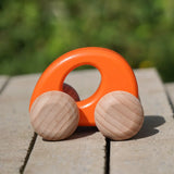 Bajo handmade wooden ellipse toy car in orange with unpainted wheels standing on a concrete surface