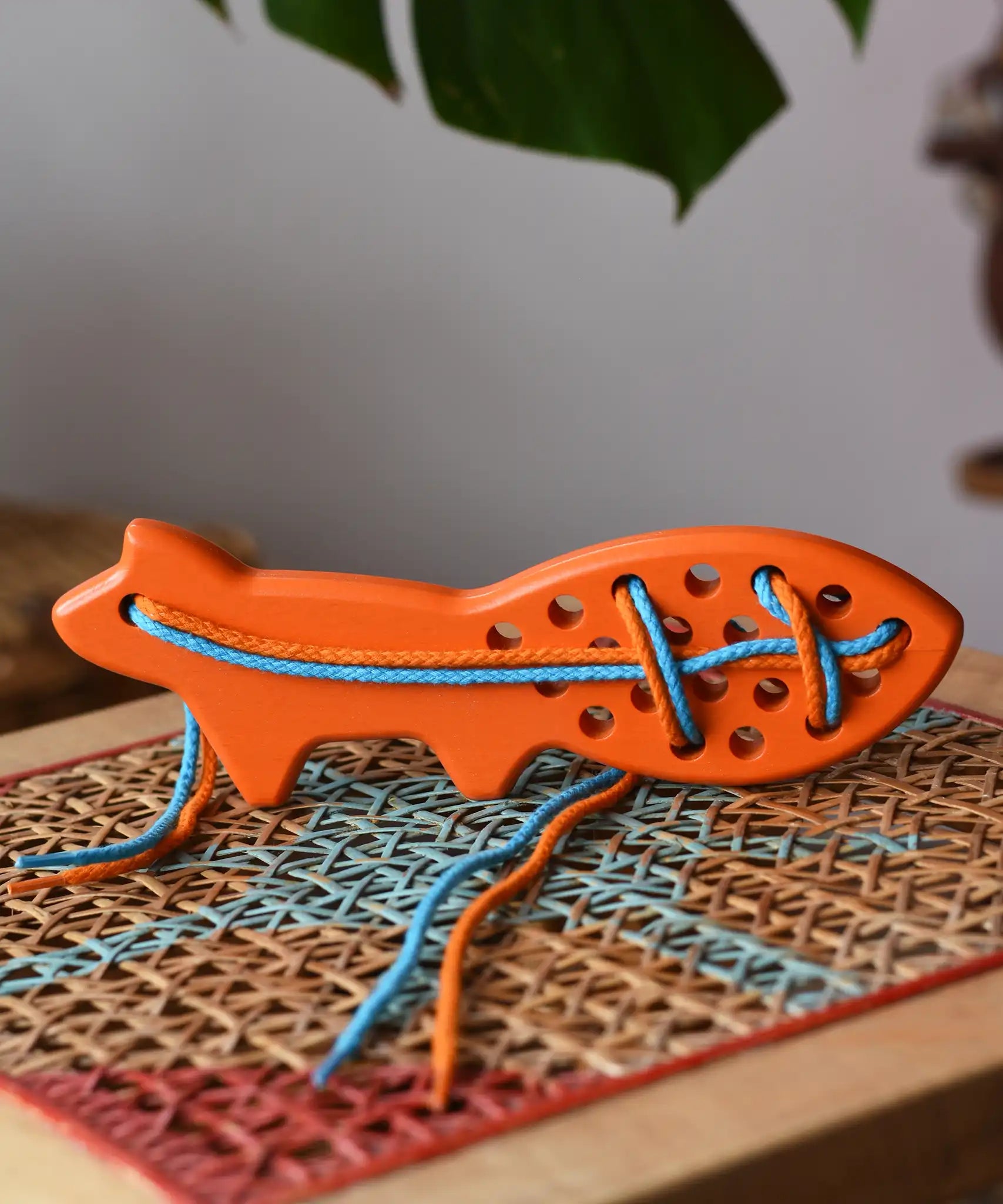 Bajo orange lacing fox wooden toy placed on a rattan stool in the Babipur playroom.
