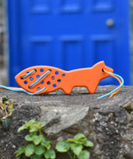 Bajo orange lacing fox wooden toy placed on a stone wall. 