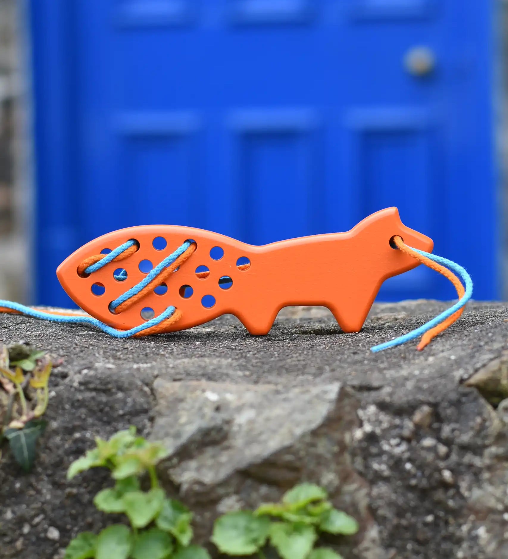 Bajo orange lacing fox wooden toy placed on a stone wall. 