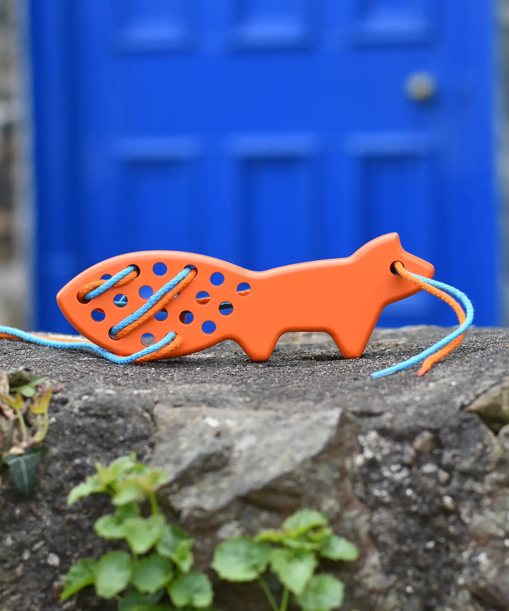 Bajo orange lacing fox wooden toy placed on a stone wall. 