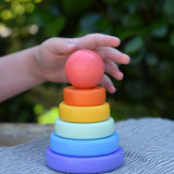 Child's hand reaching for the top ball shaped pieced from the Bajo pastel stacking rings wooden toy. 