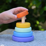 Child hand placing the orange ring onto the Bajo pastel stacking rings wooden toy. 