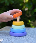 Child hand placing the orange ring onto the Bajo pastel stacking rings wooden toy. 