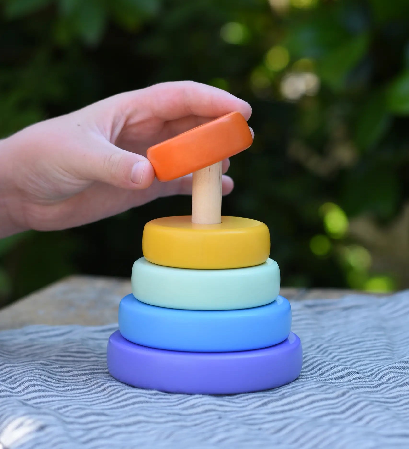 Child hand placing the orange ring onto the Bajo pastel stacking rings wooden toy. 