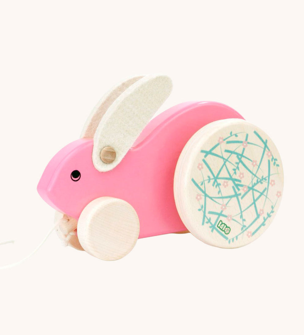 A pink Bajo Big Rabbit toy. This pull along wooden toy has small wheels at the front and large decorated wheels at the back. The rabbit makes a jumping motion as it is being pulled along. We have a wide range of Bajo wooden toys available here at Babipur. 