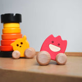 A pink coloured Bajo wooden ghost toy placed on Triclimb Miri slide. A yellow ghost and a red rook tower stacking toy can be seen in the background.  The toy has a pink painted body and natural wooden wheels. These heirloom quality toys by Bajo are part of a wide range of wooden toys available here at Babipur. 
