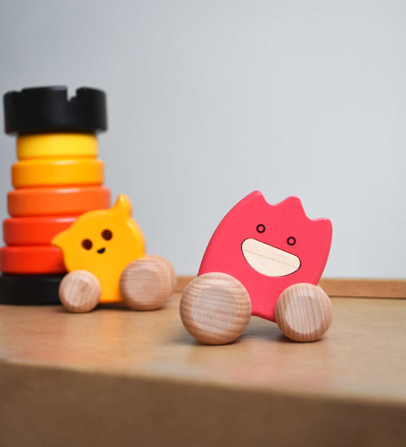 A pink coloured Bajo wooden ghost toy placed on Triclimb Miri slide. A yellow ghost and a red rook tower stacking toy can be seen in the background.  The toy has a pink painted body and natural wooden wheels. These heirloom quality toys by Bajo are part of a wide range of wooden toys available here at Babipur. 