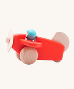 A Bajo coral wooden plane toy with pilot. The coral red coloured plane has natural wheels, propeller and tail and a blue coloured pilot. This plane is part of a wide range of Bajo wooden toy vehicles available at Babipur.