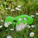 A green coloured Bajo wooden airplane with windows placed on the grass surrounded by daisies.