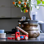 Bajo eco friendly wooden fire truck toy on a marble kitchen worktop in front of a metal flower pot