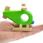 Close up of a Bajo wooden helicopter toy in the palm of a hand on a white background