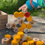 Close up of a child's hand stacking the Bajo wooden Waldorf hive blocks on a wooden log