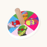 A Bajo Pop Art wooden Spinning Top toy. A white painted body with a natural wooden stick. The top of the spinning top has a colourful pop are design featuring the face of Mr Bajor.