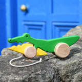 Bajo pull along crocodile wooden toy placed on a stone wall outdoors.