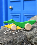 Bajo pull along crocodile wooden toy placed on a stone wall outdoors.