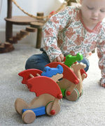 A child playing with the Bajo green pull along dragon wooden toy, the blue dragon has been placed in front of them. The dragon toy features two wheels at the front and back and red wing that move along with the front wheels. These heirloom quality toys by Bajo are part of a wide range of wooden toys available here at Babipur.