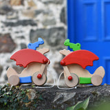 One blue and one green Bajo pull along dragon toys placed on a stone wall outdoors. These heirloom quality toys by Bajo are part of a wide range of wooden toys available here at Babipur. 