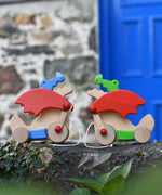 One blue and one green Bajo pull along dragon toys placed on a stone wall outdoors. These heirloom quality toys by Bajo are part of a wide range of wooden toys available here at Babipur. 