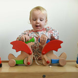 A child playing with the Bajo green and blue pull along dragon wooden toys on a Triclimb Miri slide. The dragon toys feature two wheels at the front and back and red wing that move along with the front wheels. These heirloom quality toys by Bajo are part of a wide range of wooden toys available here at Babipur.