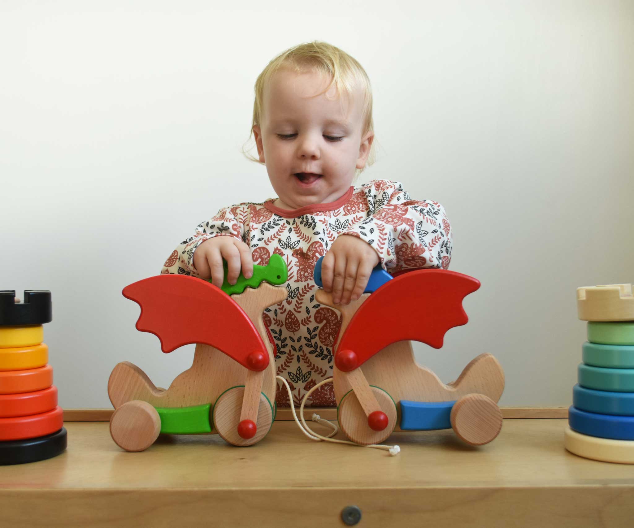 A child playing with the Bajo green and blue pull along dragon wooden toys on a Triclimb Miri slide. The dragon toys feature two wheels at the front and back and red wing that move along with the front wheels. These heirloom quality toys by Bajo are part of a wide range of wooden toys available here at Babipur.