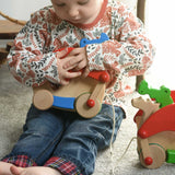 A child cuddling the Bajo blue pull along dragon wooden toy.  The dragon toy features two wheels at the front and back and red wing that move along with the front wheels. These heirloom quality toys by Bajo are part of a wide range of wooden toys available here at Babipur.