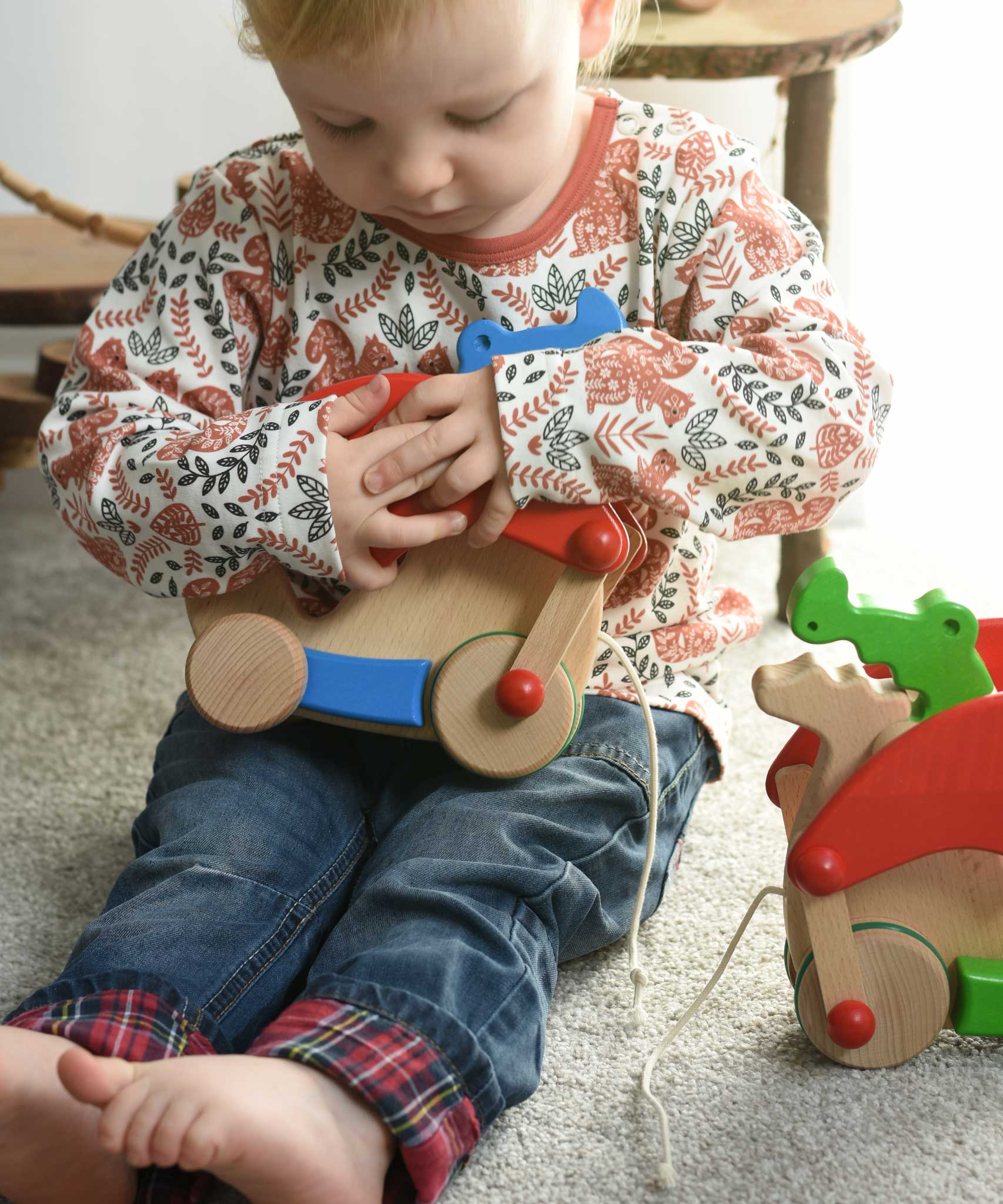 A child cuddling the Bajo blue pull along dragon wooden toy.  The dragon toy features two wheels at the front and back and red wing that move along with the front wheels. These heirloom quality toys by Bajo are part of a wide range of wooden toys available here at Babipur.