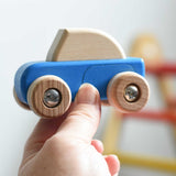 A blue coloured Bajo pull back action wooden toy car held up in an adult's hand. These heirloom quality toys by Bajo are part of a wide range of wooden toys available here at Babipur. 