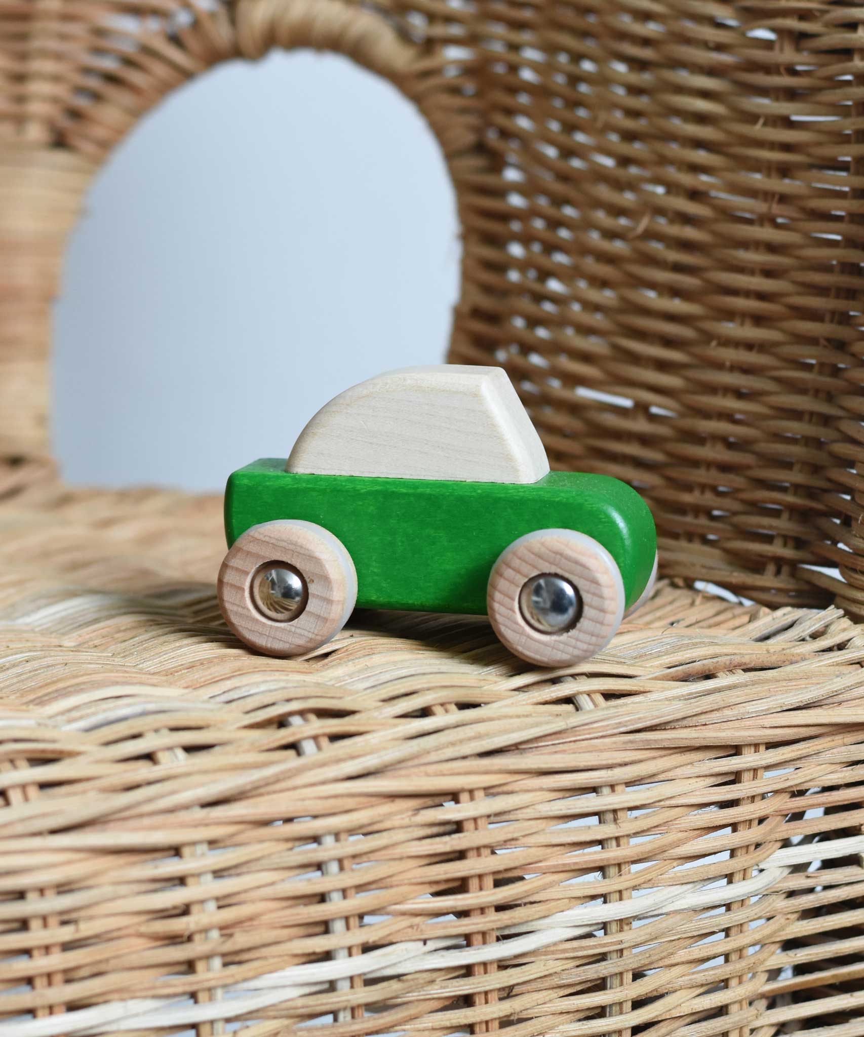A green coloured Bajo pull back action toy wooden car placed on a child's wicker chair. These heirloom quality toys by Bajo are part of a wide range of wooden toys available here at Babipur. 