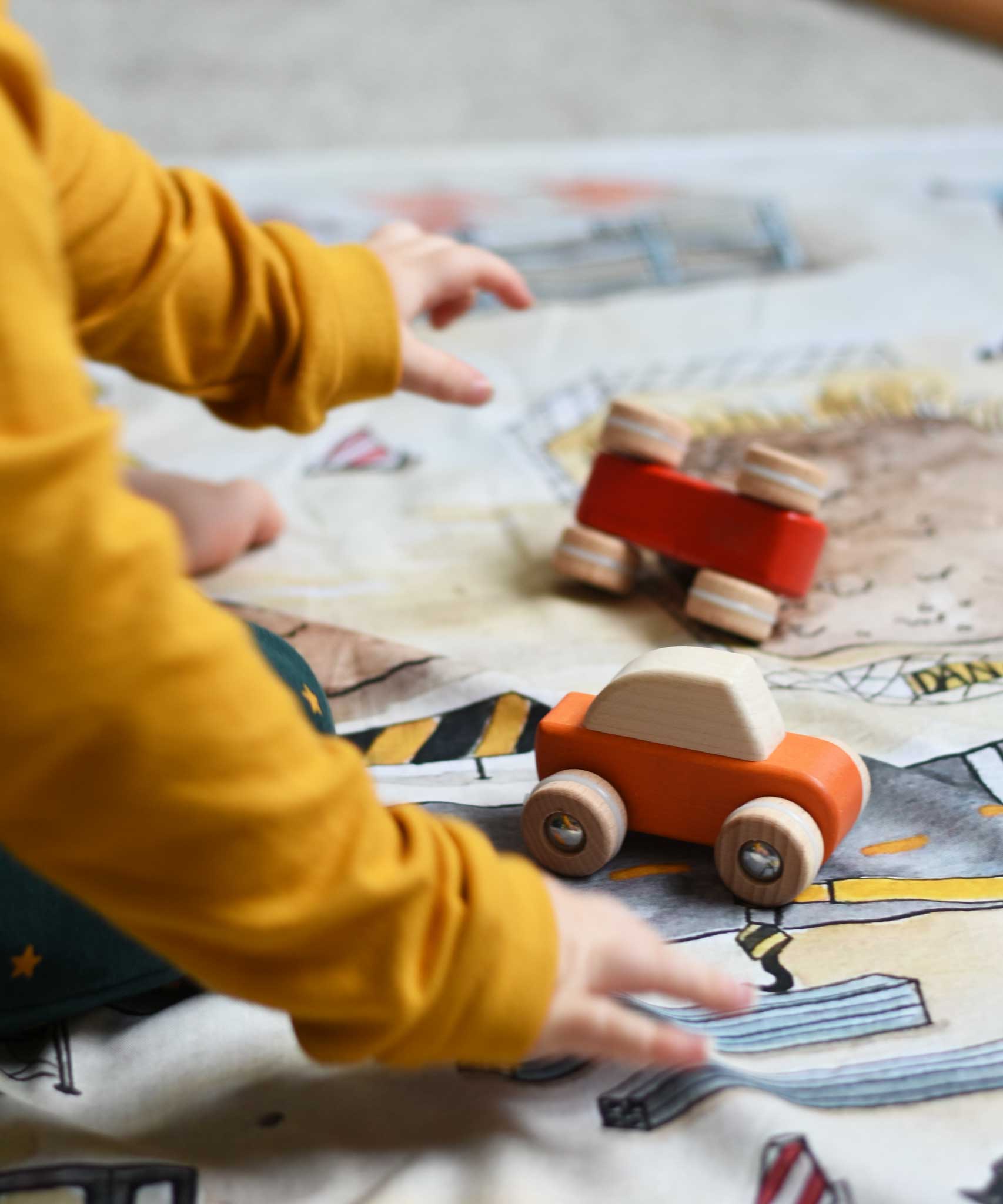 A close up of a child playing with the Bajo pull back action wooden toy cars. The cars have been placed on the road printed on the Wonderie building site cloth. A child playing with the Bajo racing cars that have been placed on a Wonderie building site play cloth. These heirloom quality toys by Bajo are part of a wide range of wooden toys available here at Babipur. 