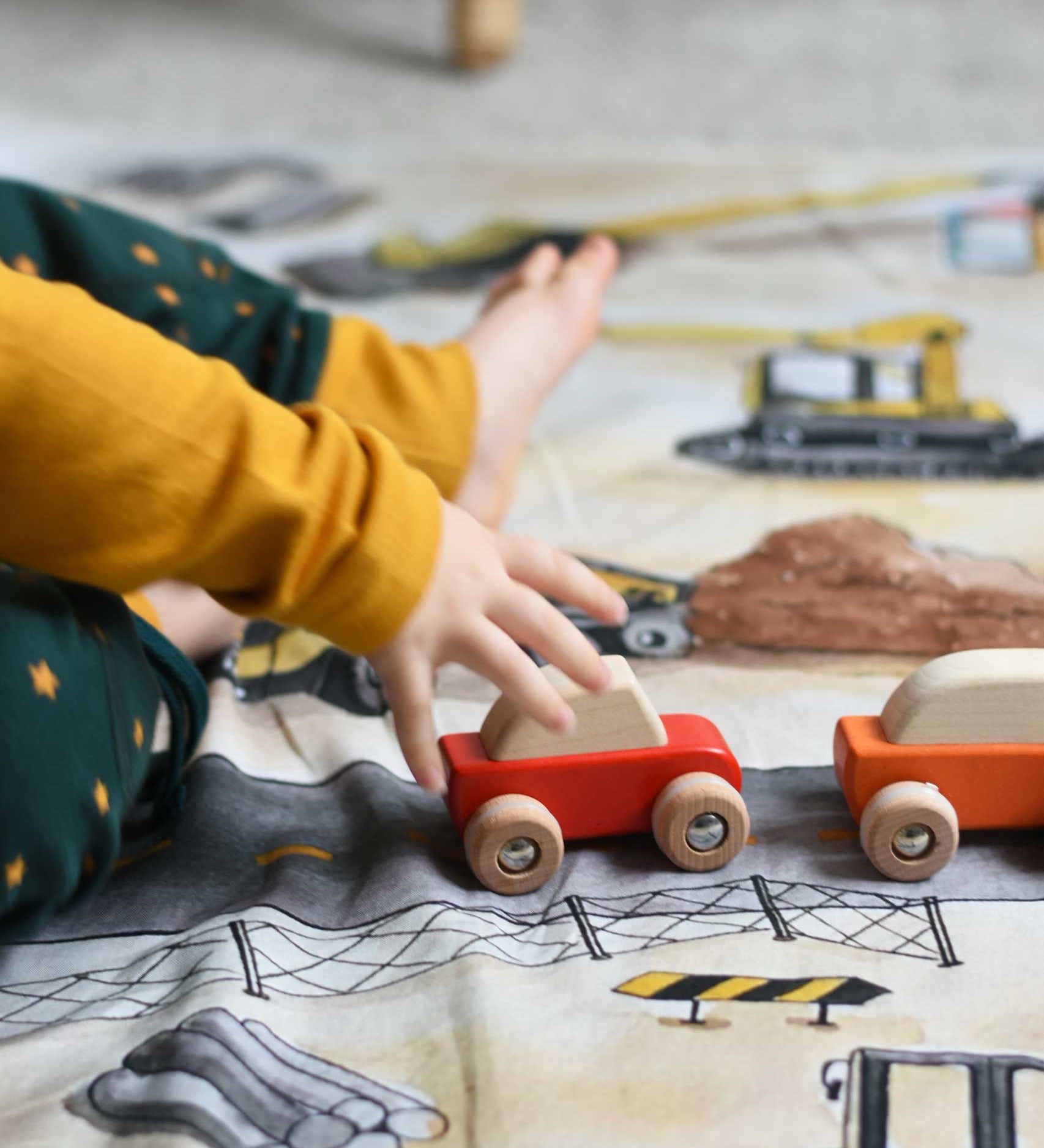A close up of a child playing with the Bajo pull back action wooden toy cars. The cars have been placed on the road printed on the Wonderie building site cloth. A child playing with the Bajo racing cars that have been placed on a Wonderie building site play cloth. These heirloom quality toys by Bajo are part of a wide range of wooden toys available here at Babipur. 