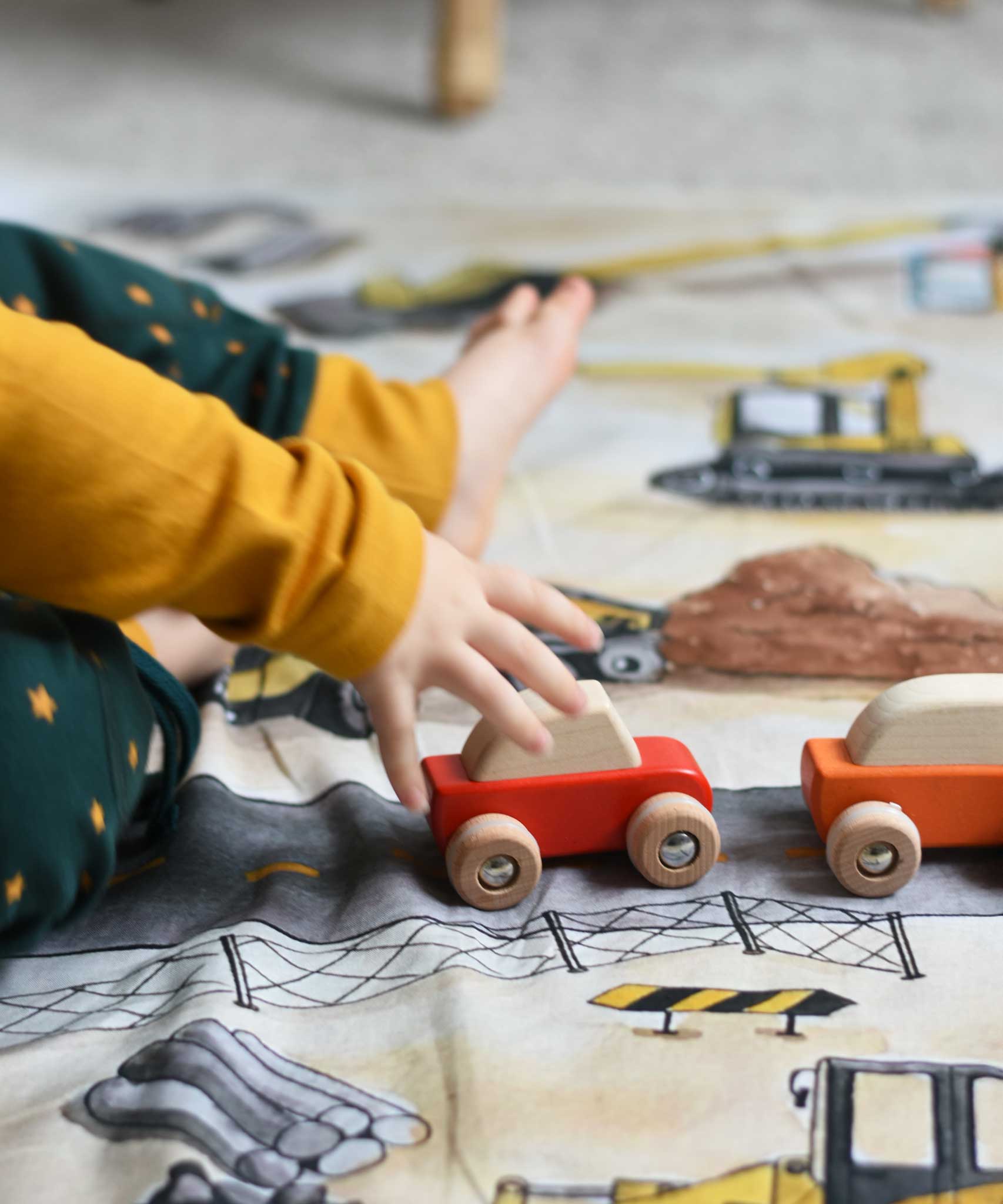 A close up of a child playing with the Bajo pull back action wooden toy cars. The cars have been placed on the road printed on the Wonderie building site cloth. A child playing with the Bajo racing cars that have been placed on a Wonderie building site play cloth. These heirloom quality toys by Bajo are part of a wide range of wooden toys available here at Babipur. 