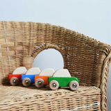 Four Bajo pull back action wooden toy cars placed on a child's wicker chair. These heirloom quality toys by Bajo are part of a wide range of wooden toys available here at Babipur. 