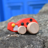 Bajo pull-back ladybird wooden toy figure on wheels placed on a stone wall.
