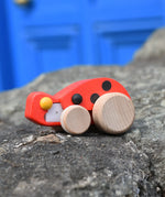 Bajo pull-back ladybird wooden toy figure on wheels placed on a stone wall.