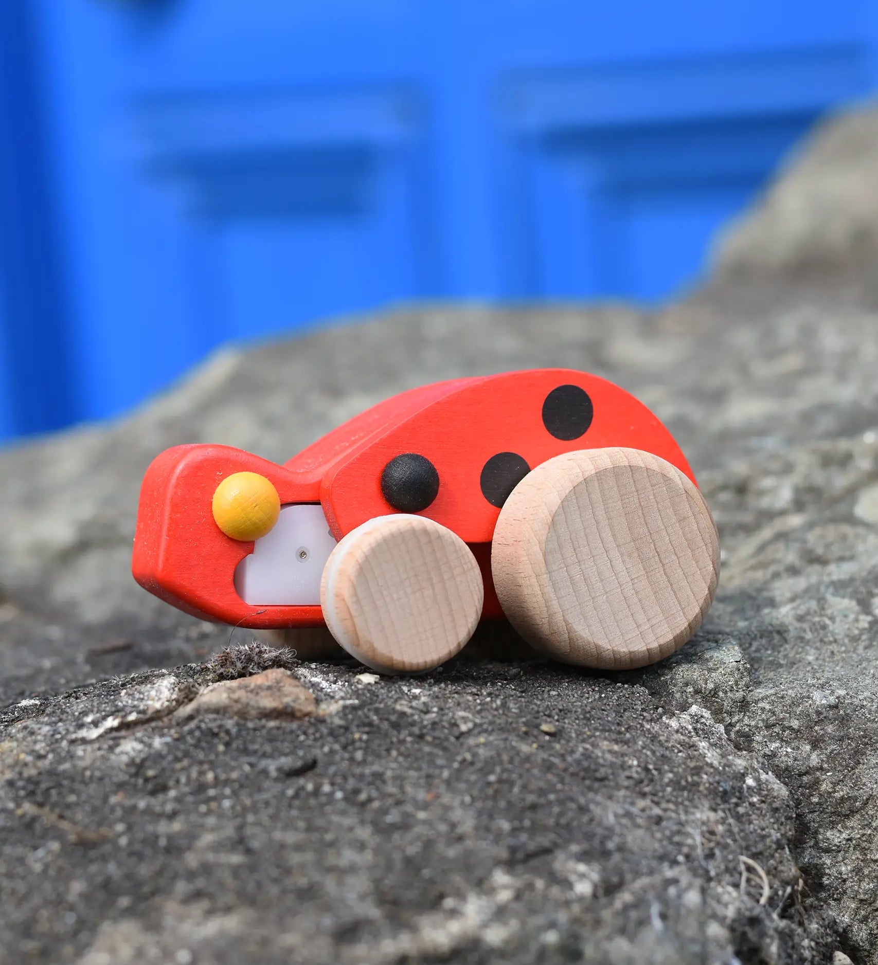 Bajo pull-back ladybird wooden toy figure on wheels placed on a stone wall.