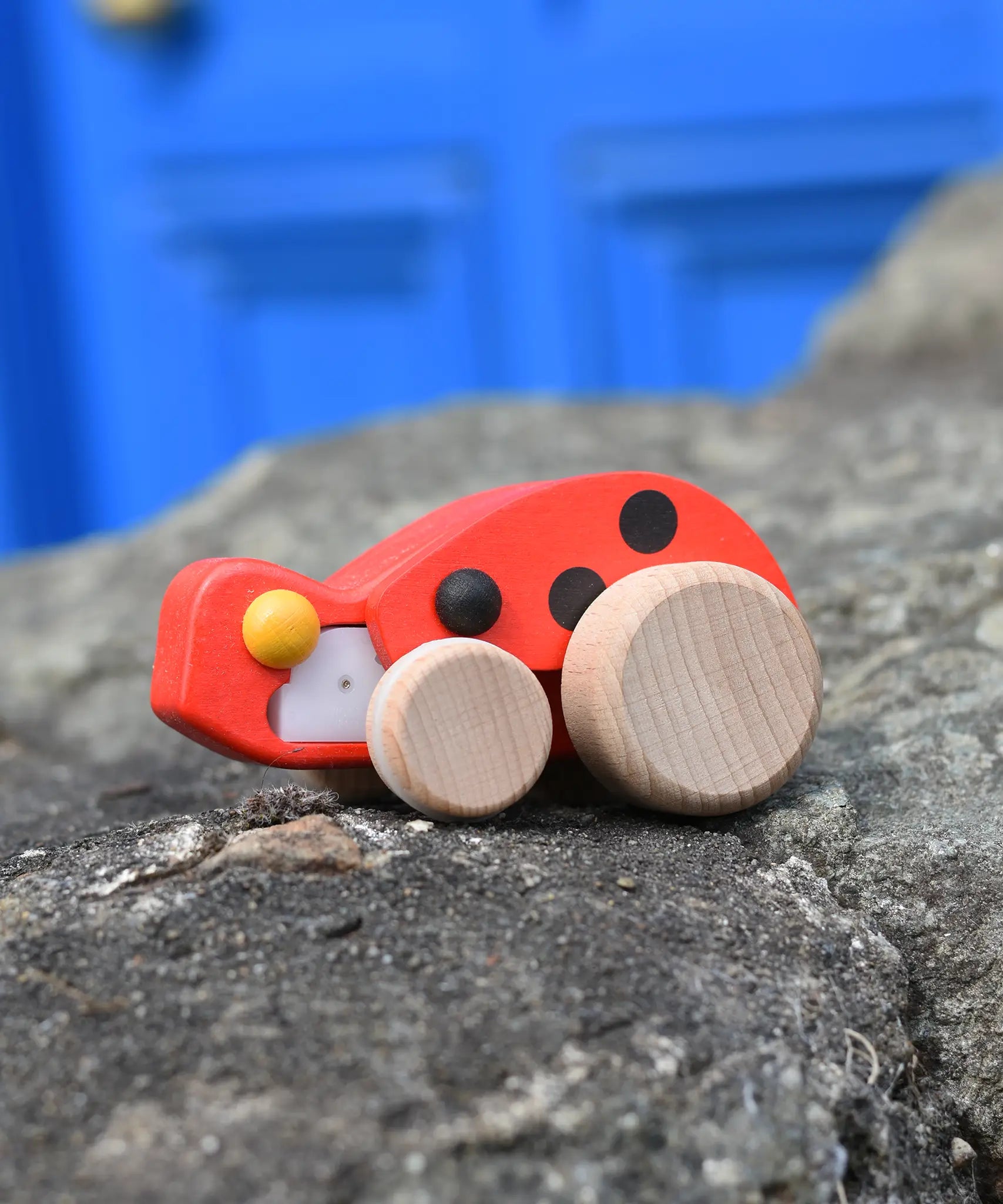Bajo pull-back ladybird wooden toy figure on wheels placed on a stone wall.